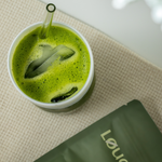 Løuco green protein smoothie in a cup with a straw on a textured surface, next to a Løuco Nourish package.