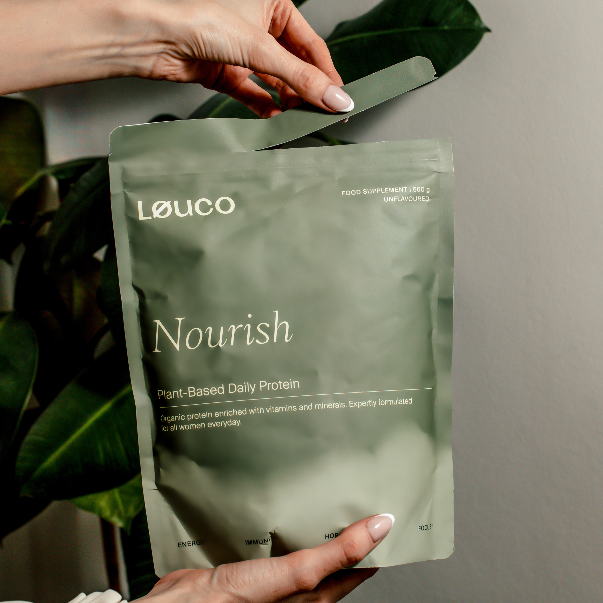 Person holding a Løuco Nourish plant-based daily protein package against a neutral background.