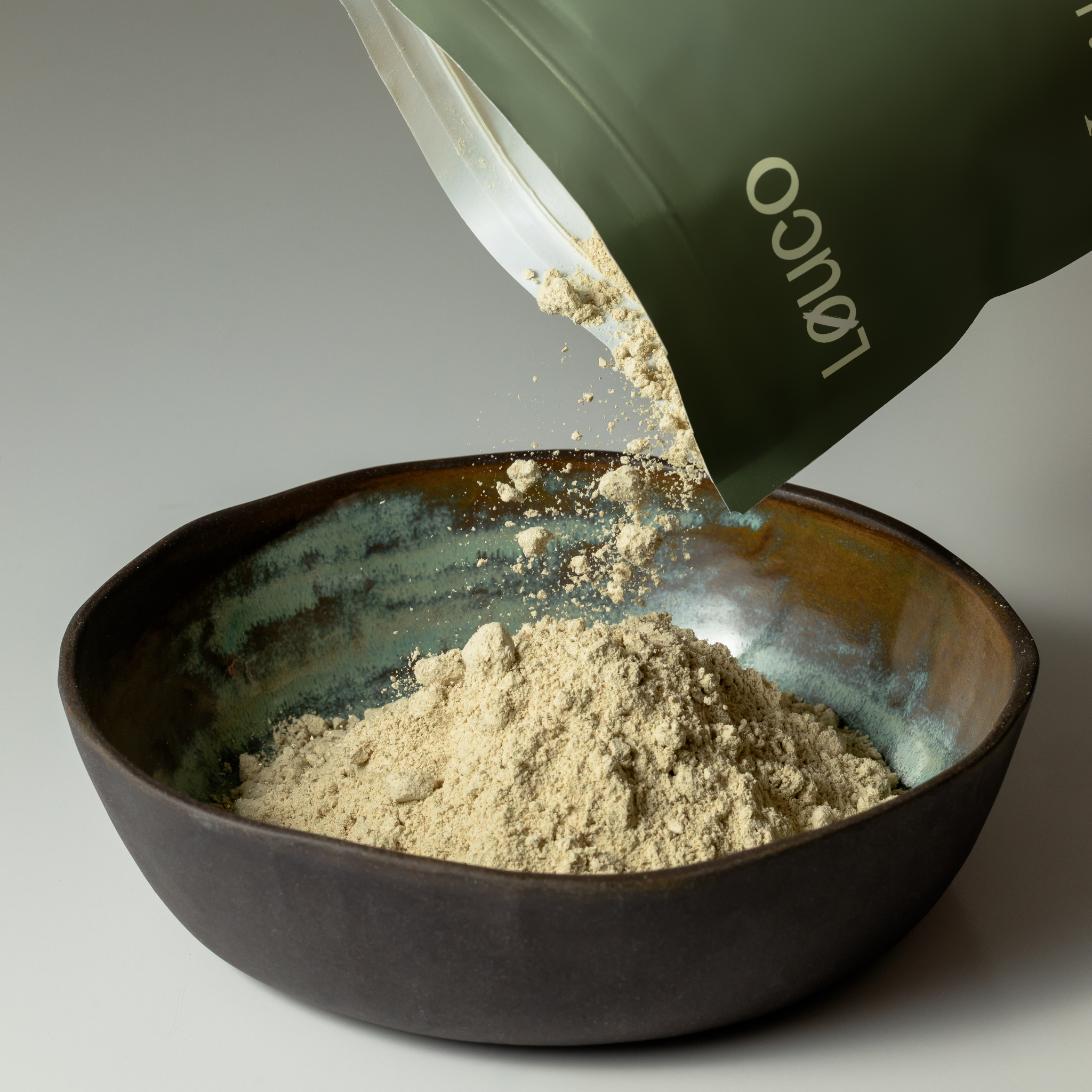 Løuco Nourish Protein Powder being poured from a green pouch into a dark bowl.