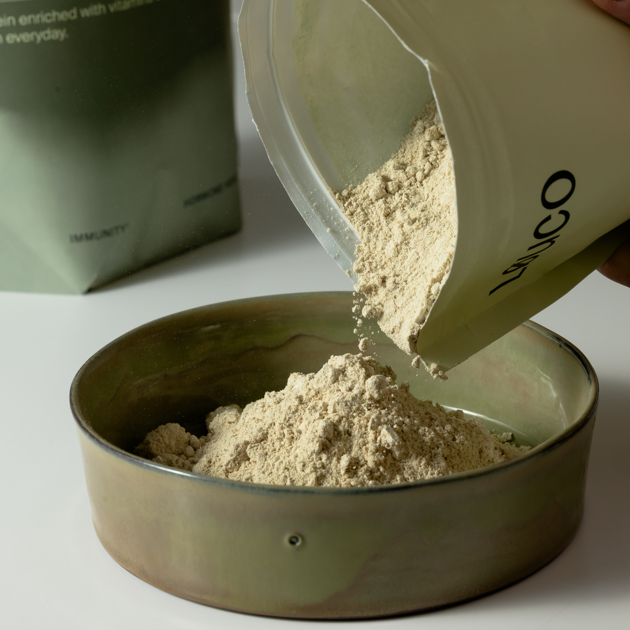 LØUCO Perform protein powder being poured from a container into a bowl on a light background