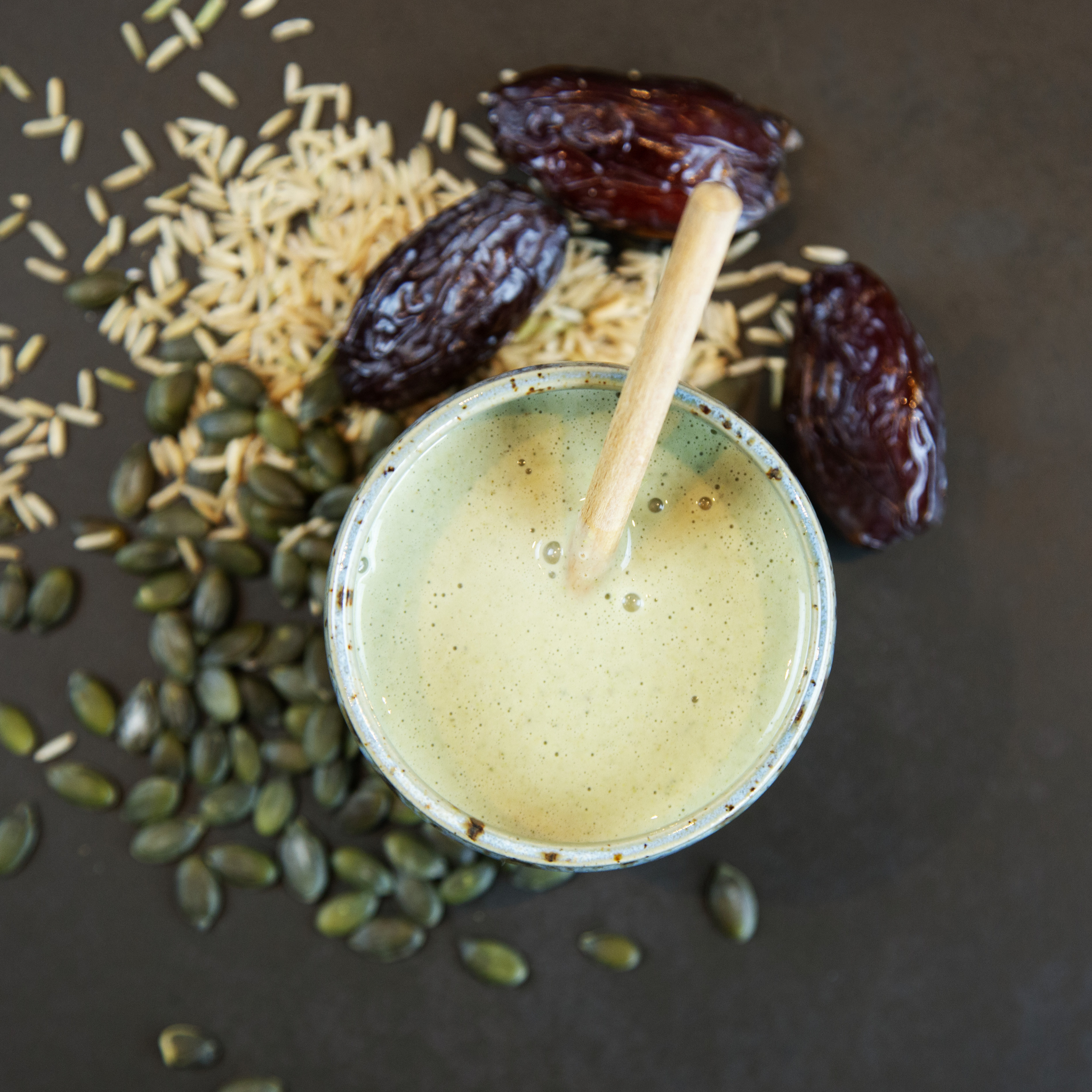 Løuco green smoothie in a cup with dates and pumpkin seeds on a dark surface