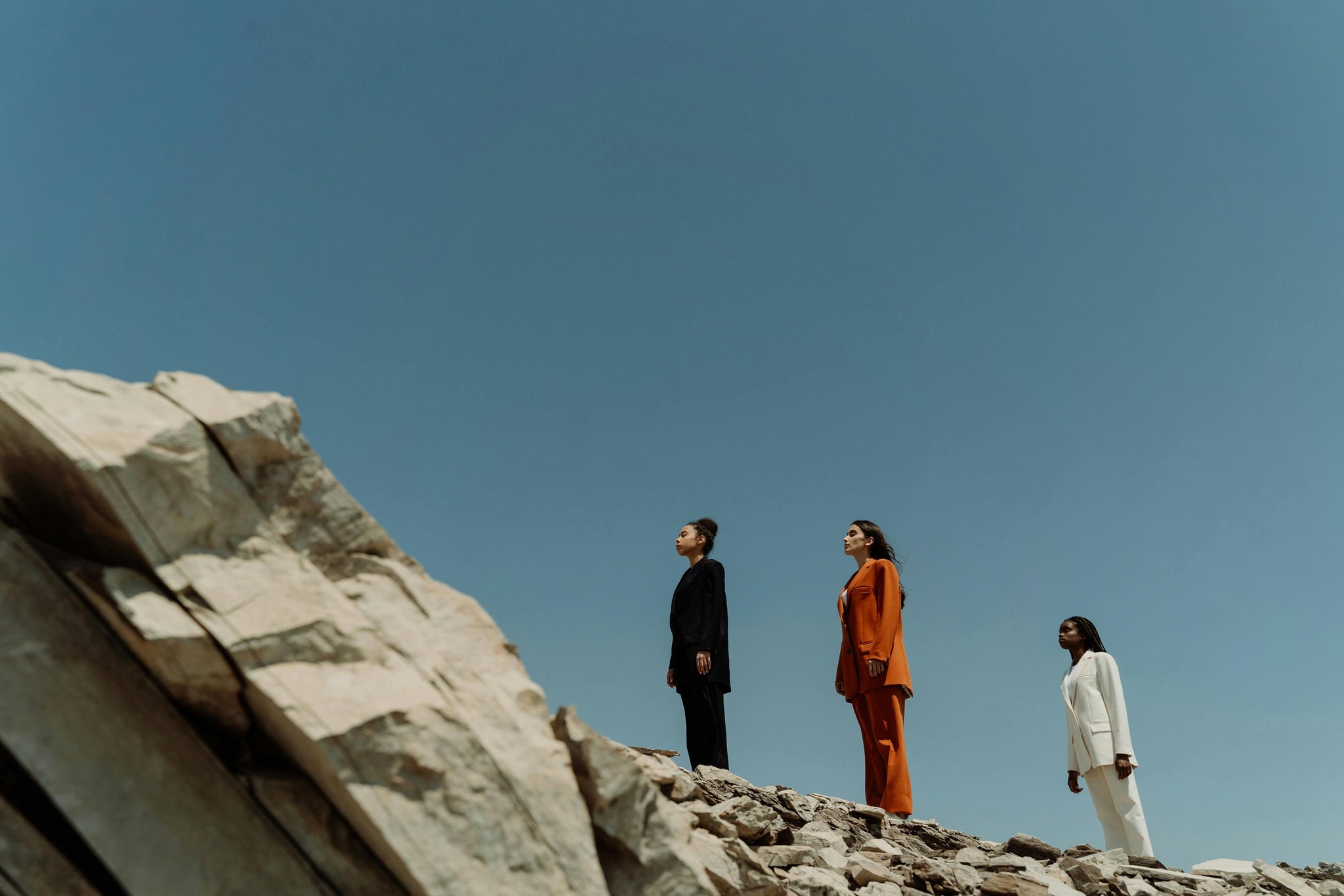 Three empowered women standing on a rocky outcrop against a clear blue sky.